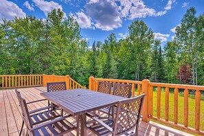 A wooden deck with a table and chairs, surrounded by a wooden railing, overlooking a forested area. - Peaceful North Haverhill Haven w/ Wood Fire Pit (North Haverhill)