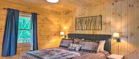 Ett sovrum med träpanel på väggarna, en säng, två sänglampor, en takfläkt och ett fönster med gardiner.