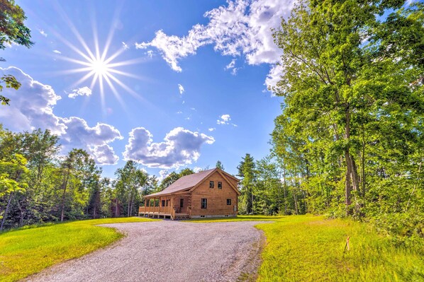 A wooden cabin with a gravel driveway, surrounded by lush greenery and trees. - Peaceful North Haverhill Haven w/ Wood Fire Pit (North Haverhill)