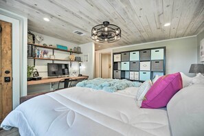 Quarto com cama, escrivaninha com computador, televisão e unidade de armazenamento com vários compartimentos.