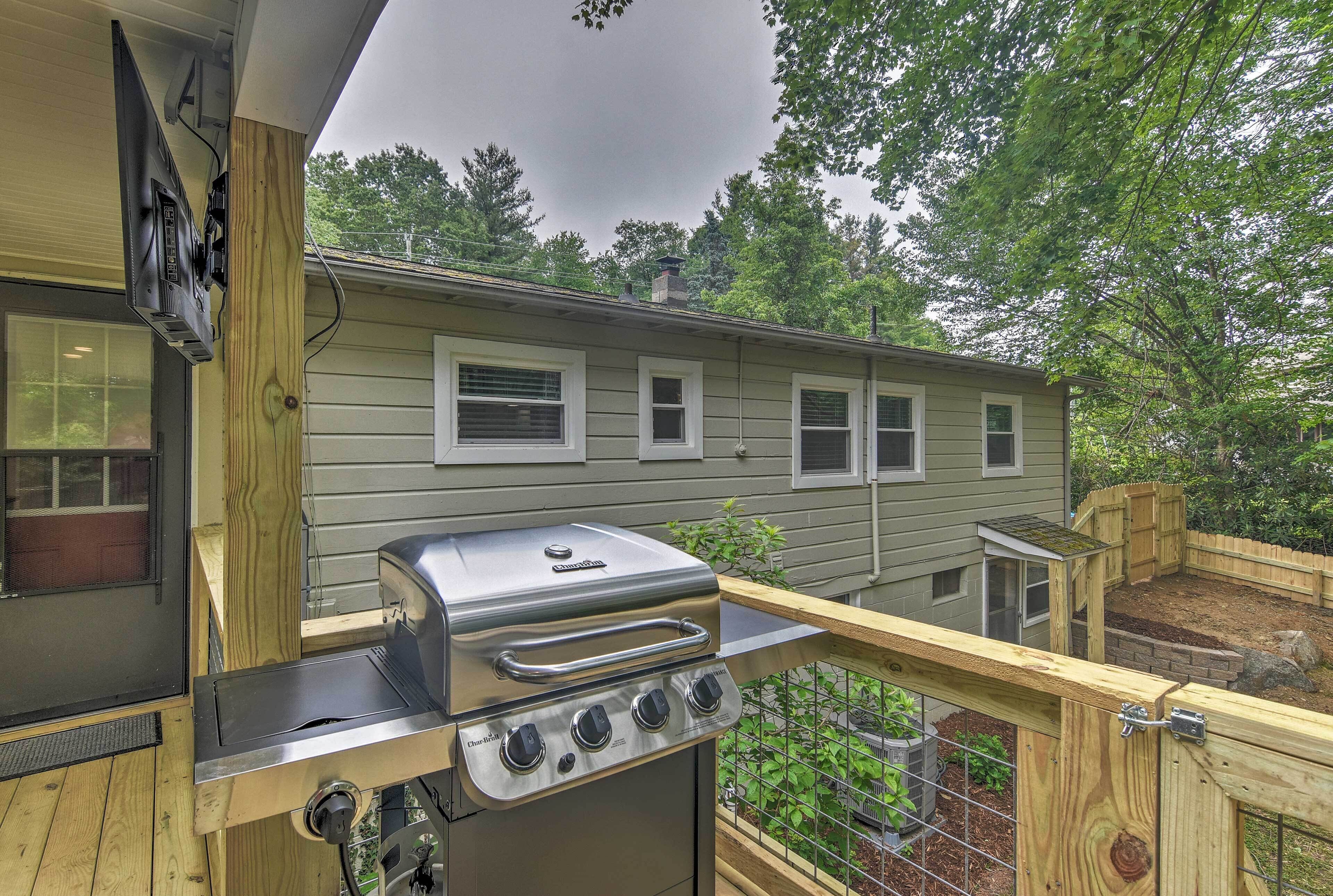 A backyard with a stainless steel grill, wooden deck, and a house with multiple windows.