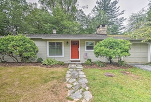 A single-story house with a red front door, stone pathway leading to the entrance, and a small front yard with trimmed bushes and a flag. - Blowing Rock Home: 1 Block to Downtown! (Blowing Rock)
