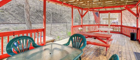 Una terraza cubierta al aire libre con una mesa y sillas, barandas de madera y vista a zona boscosa.
