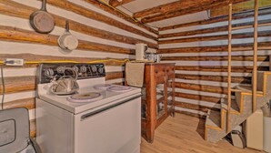 L’intérieur d’un chalet rustique, avec un mur en rondins de bois, un poêle blanc, une bouilloire, une machine à café et une échelle.