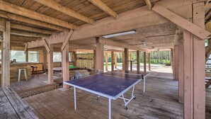 Eine Holzterrasse mit Tischtennisplatten, Sitzgelegenheiten im Freien und Blick auf den umgebenden Wald.