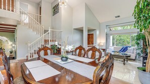 Un comedor amplio con una gran mesa de madera, sillas blancas y una escalera que sube a un nivel superior.