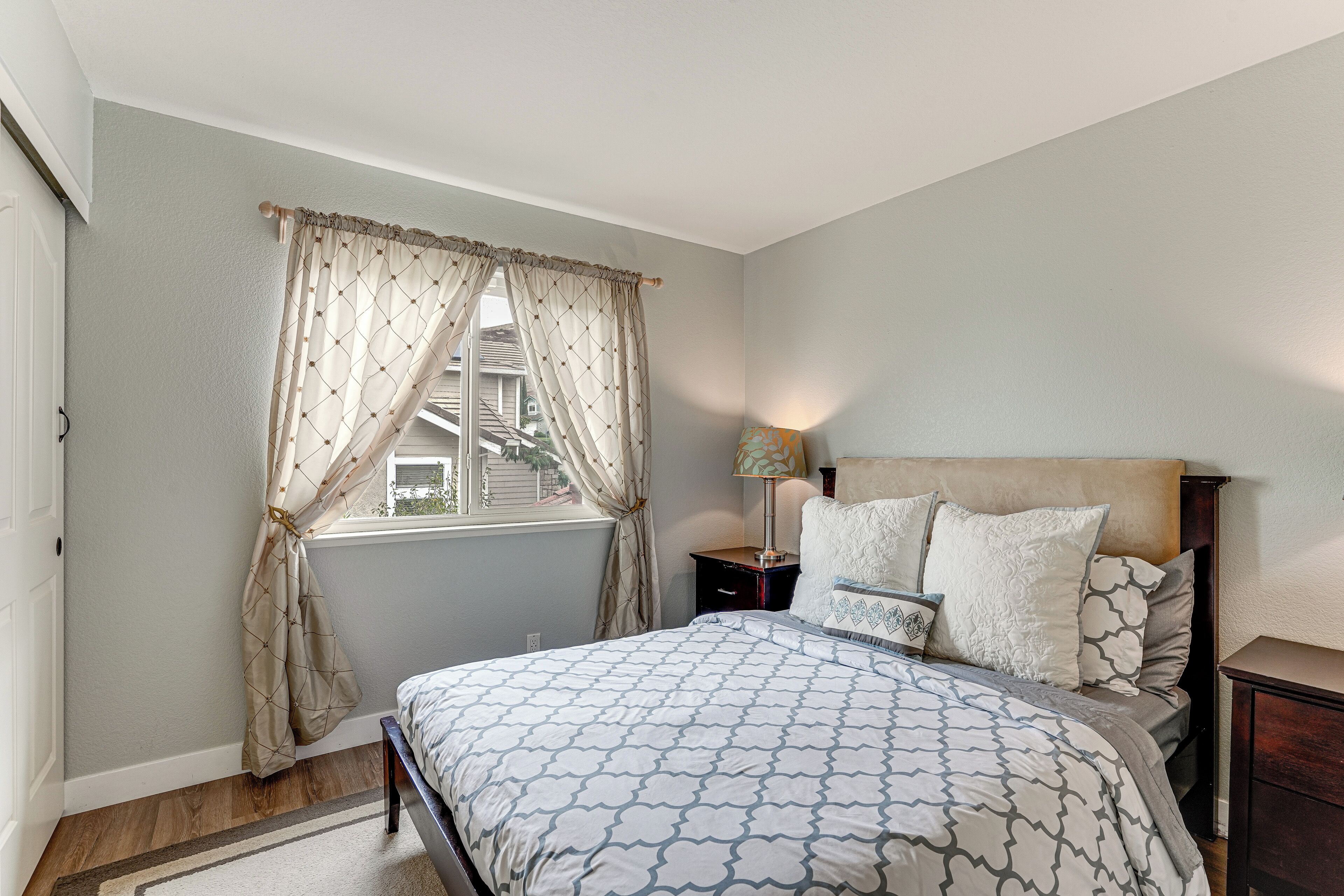 Un dormitorio con cama, mesitas de noche, lámpara y ventana con cortinas.