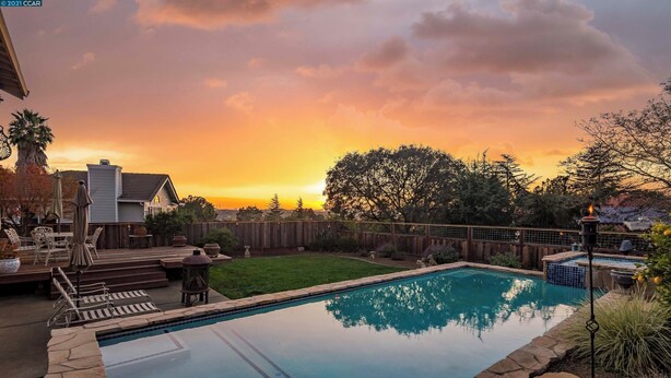 Una piscina rectangular con borde de piedra, rodeada por una terraza de madera y una zona ajardinada.
