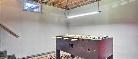 A room with a foosball table, a small window, and a ceiling fan.