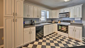 Une cuisine avec des meubles blancs, un carrelage noir et blanc, un lave-vaisselle, un four à micro-ondes et une cuisinière.
