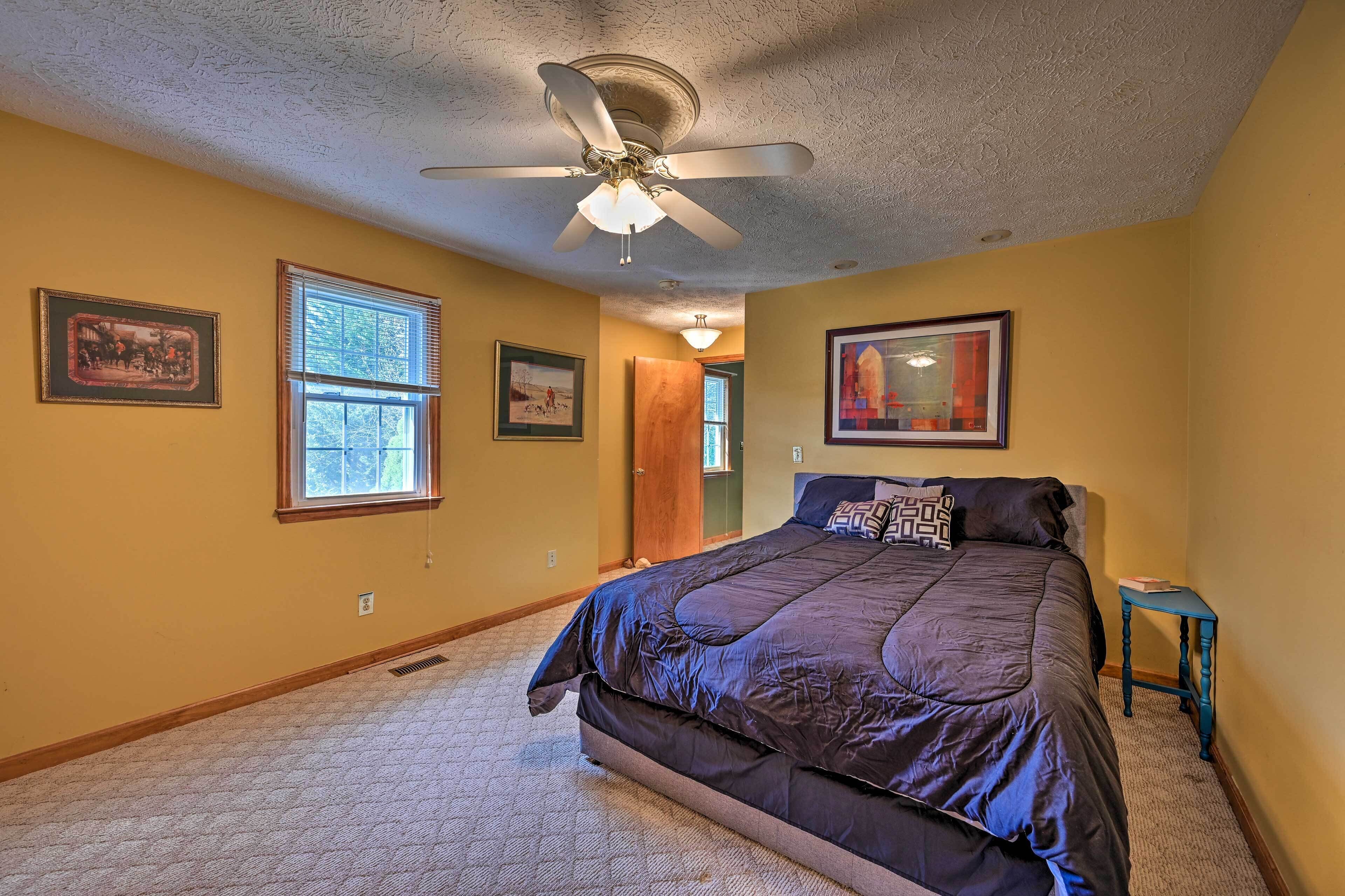 A bedroom with a large bed, a ceiling fan, and two windows.