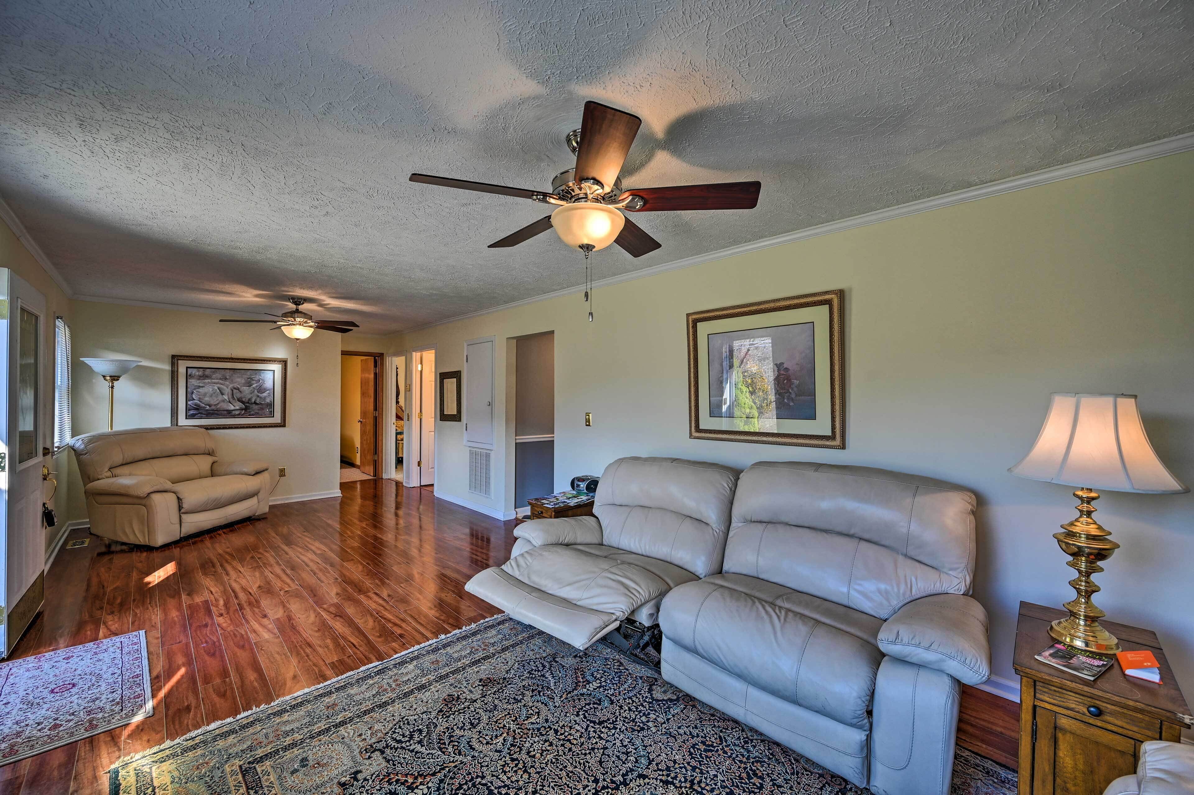 A spacious living room with a large leather sofa, a ceiling fan, and a patterned rug.