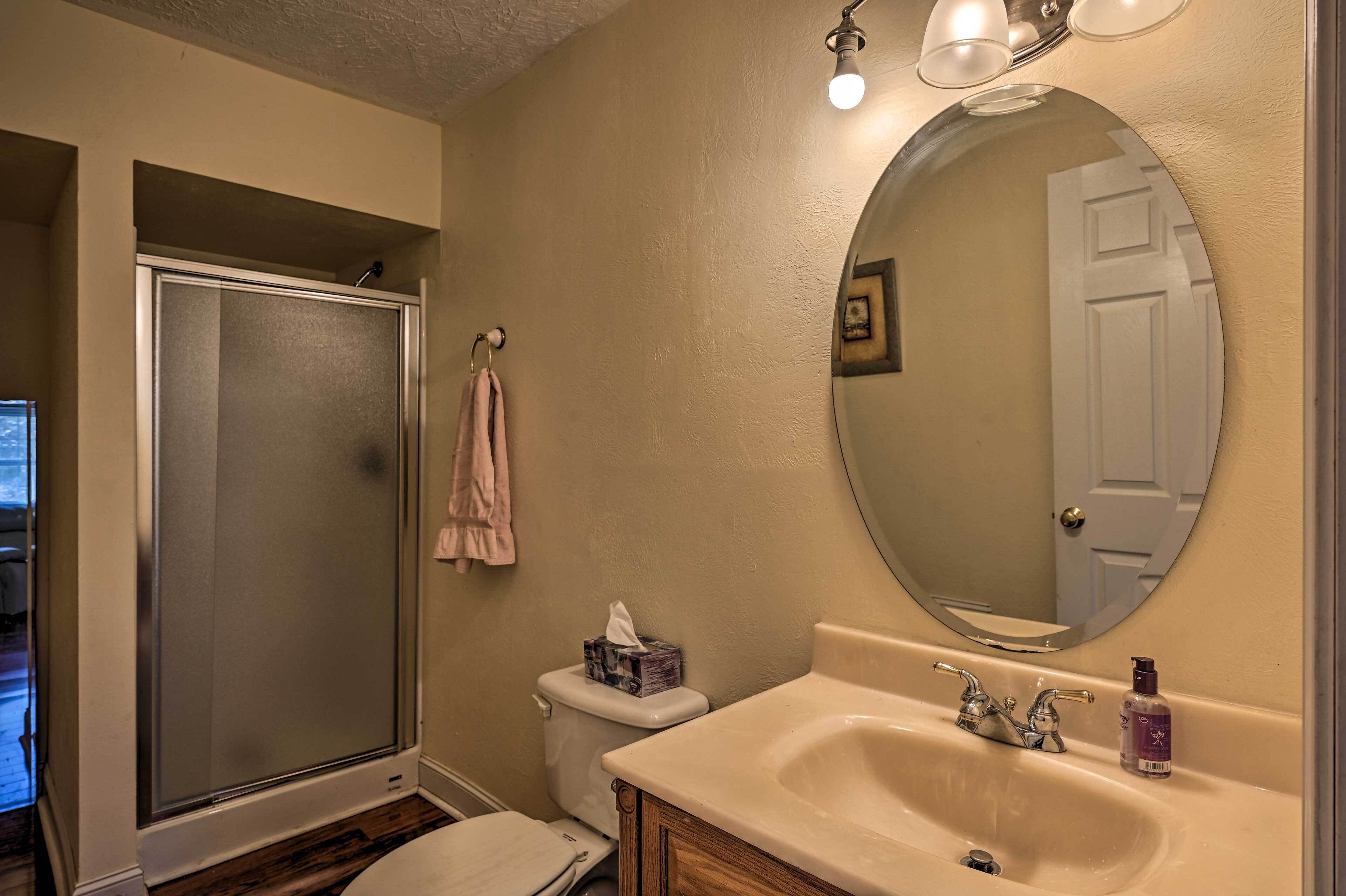 A bathroom with a shower, toilet, sink, and a large mirror.