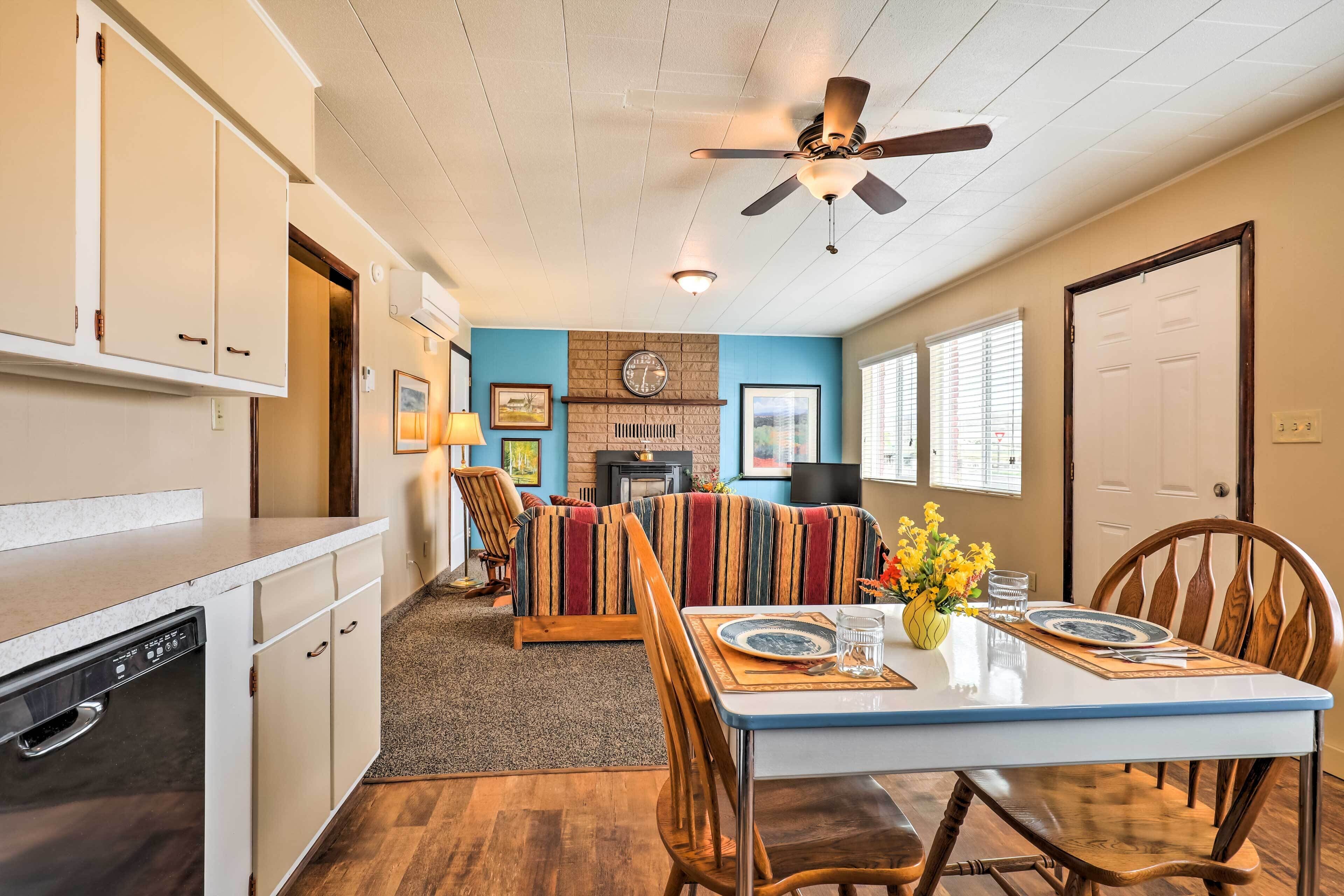 A dining area with a table set for two, a sofa, and a kitchen area with cabinets and a dishwasher.