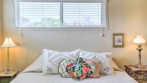 Un dormitorio con una cama, dos lámparas de noche, una ventana con persianas y un cuadro en la pared.
