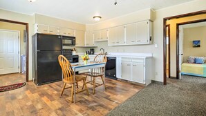 Una cocina compacta con armarios blancos, un refrigerador negro y una zona de comedor con dos sillas de madera.