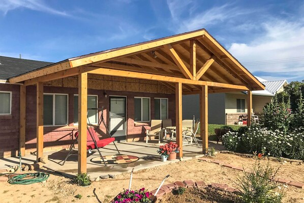 A covered patio area with a wooden roof, outdoor furniture, and a garden with flowers. - Tropic Family House - 10 Miles to Bryce Canyon! (Tropic)