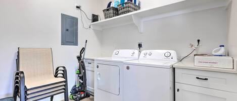 Un cuarto de lavandería con lavadora, secadora y una silla.