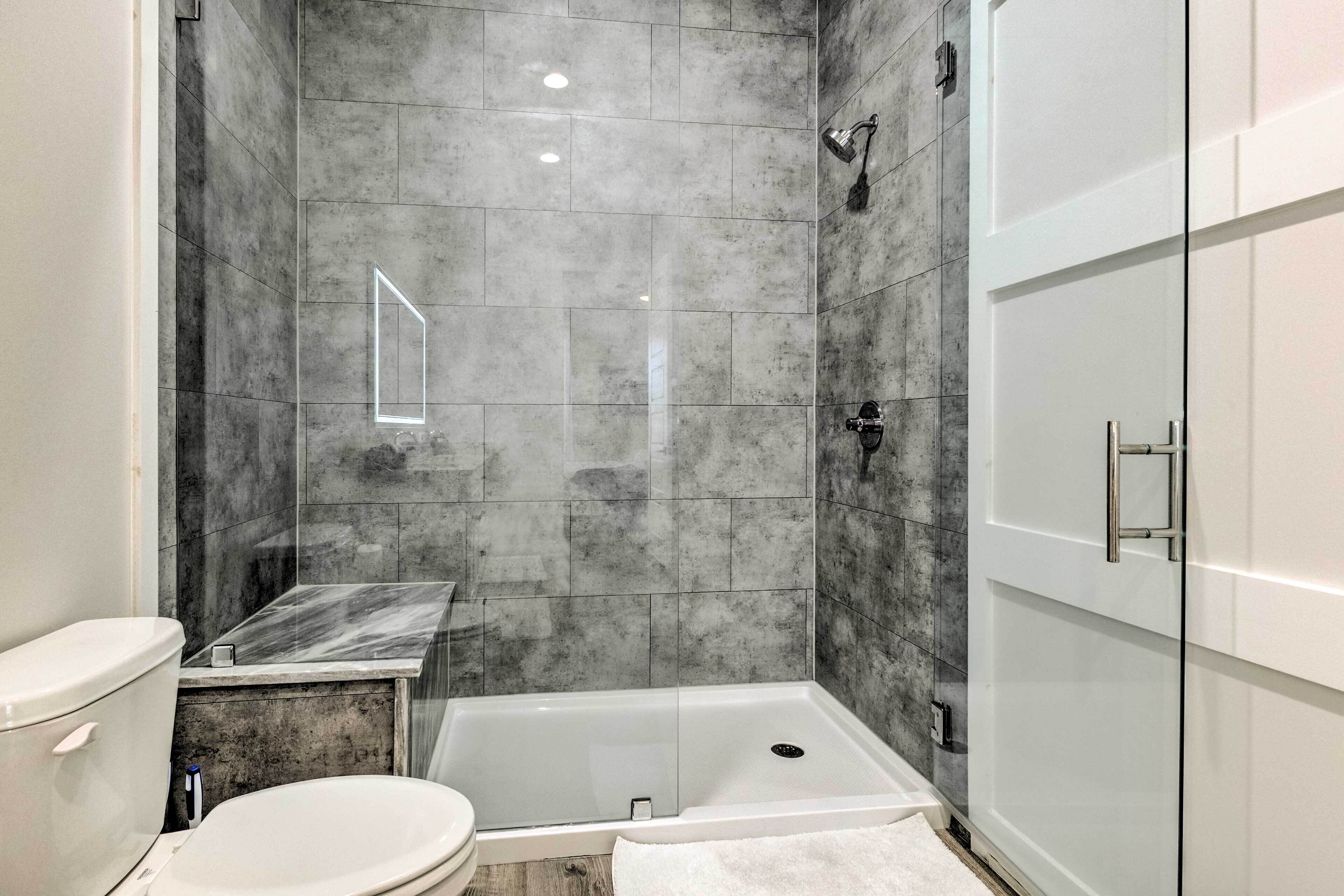 A modern bathroom with a glass-enclosed shower, a white toilet, and a marble-tiled vanity.