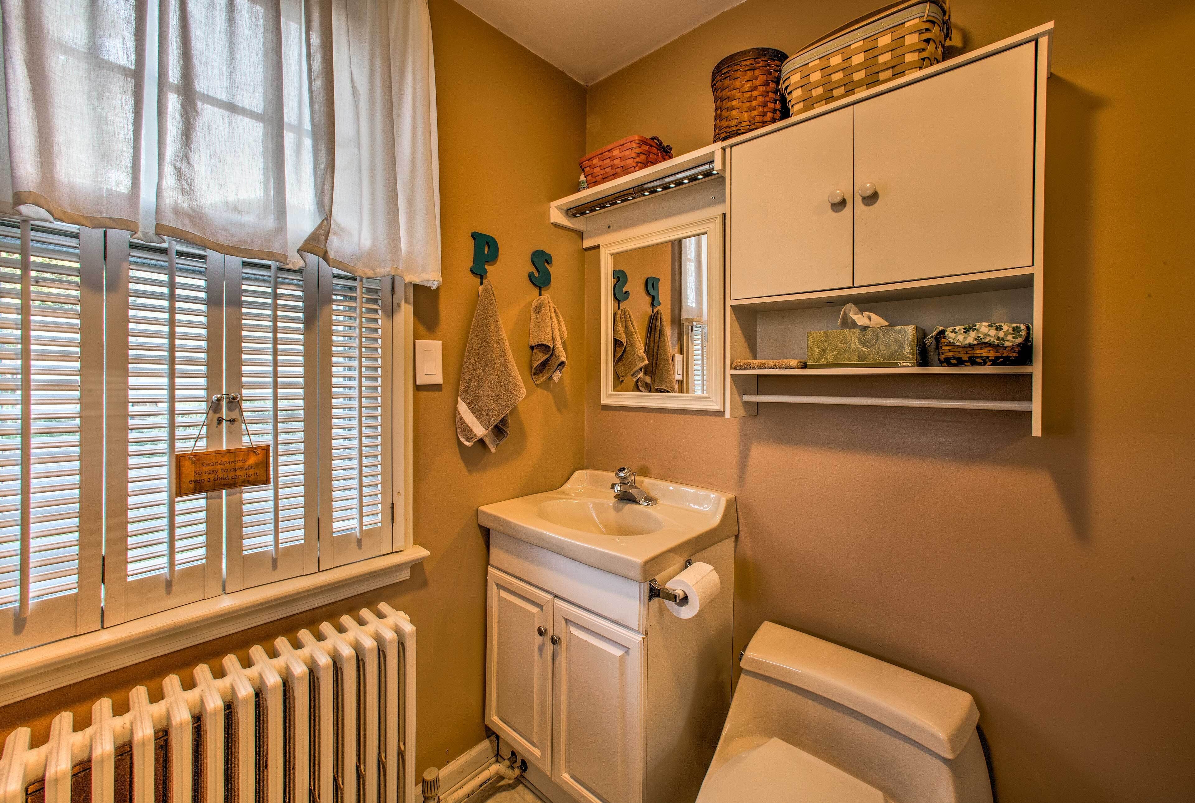 Ein Badezimmer mit Fenster, Heizkörper, Waschbecken, Spiegel und Stauraumschrank.