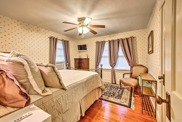 A bedroom with a bed, a desk, a chair, a ceiling fan, a TV, and a window with curtains. - Whimsical Lancaster House w/ Porch Near Amish Farm (Lancaster)