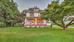 A two-story house with a front porch, a small garden, and a large tree in the front yard. - Whimsical Lancaster House w/ Porch Near Amish Farm (Lancaster)