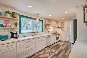 A modern kitchen with white cabinetry, a coffee maker, and a toaster. There is a window with a view of trees outside.