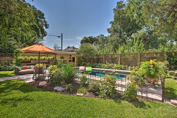 A backyard with a pool, a wooden deck, and a fenced area with plants.