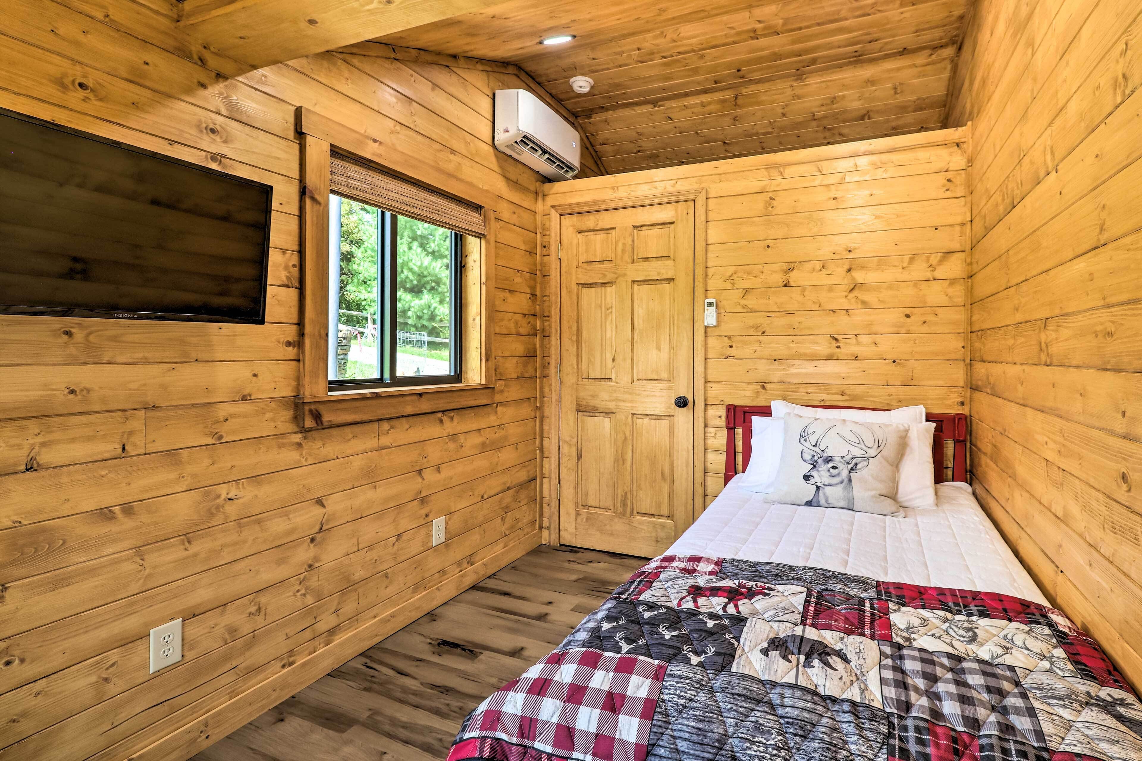 A wooden cabin room with a bed, a window, and an air conditioning unit.