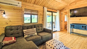 A cozy wooden cabin interior with a sectional sofa, a television, and a dining area. - Grill & River Access: Tiny Cabin in Sparta! (Sparta)
