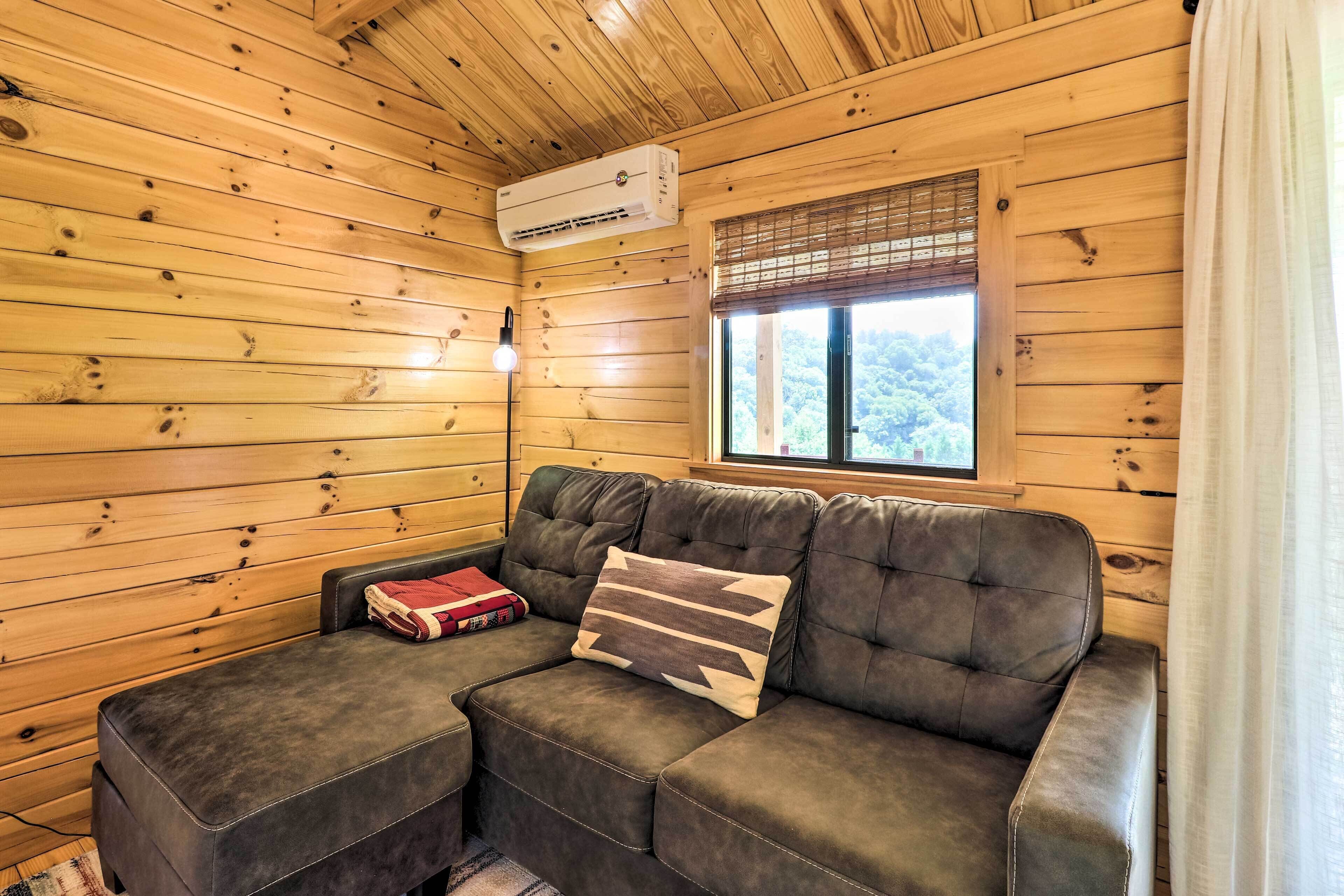 En stuga med träpanel på insidan, komplett med en soffa, en filt och ett fönster med utsikt över skogen.