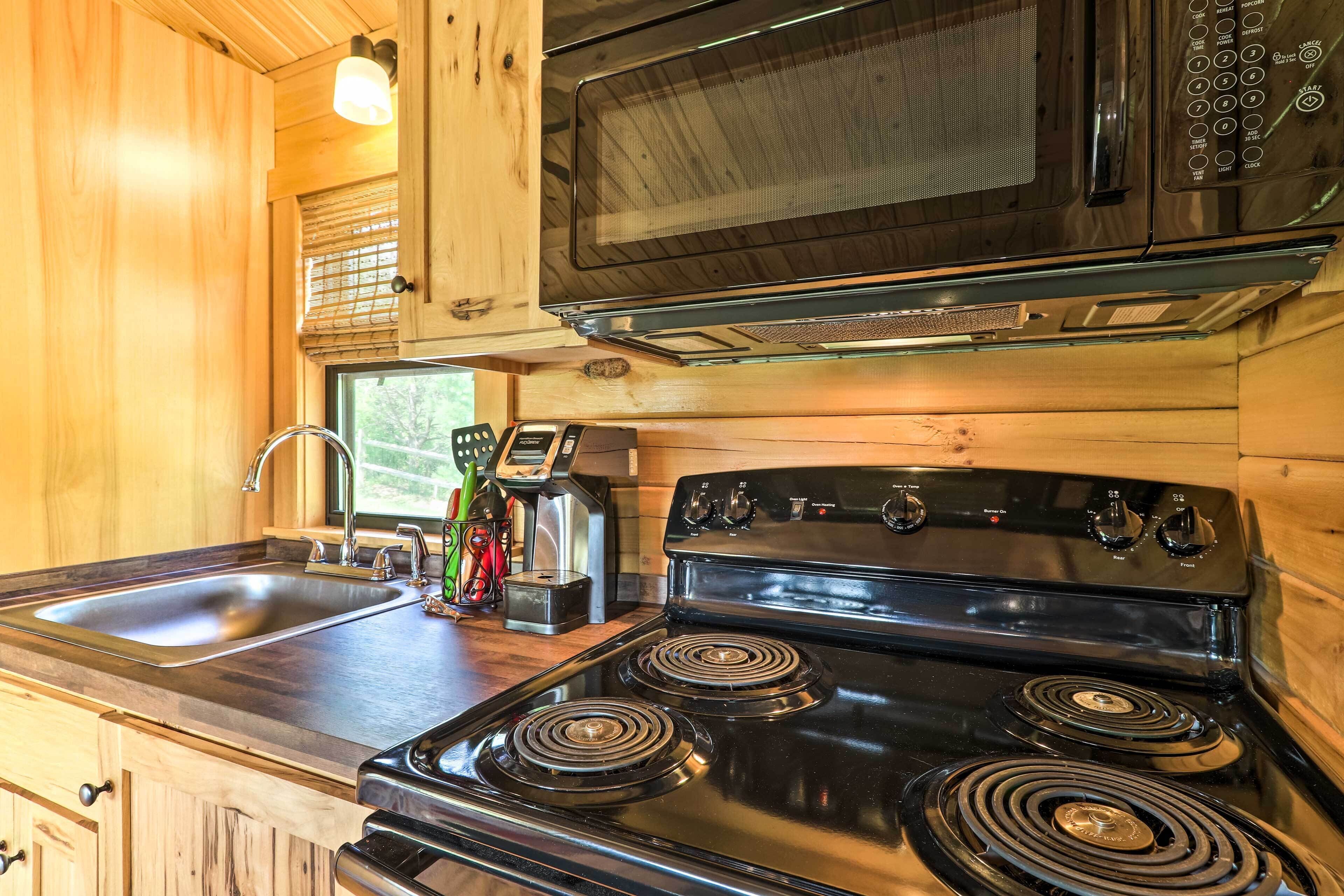 A kitchen with wooden cabinets, a black stove, a sink, and a microwave.