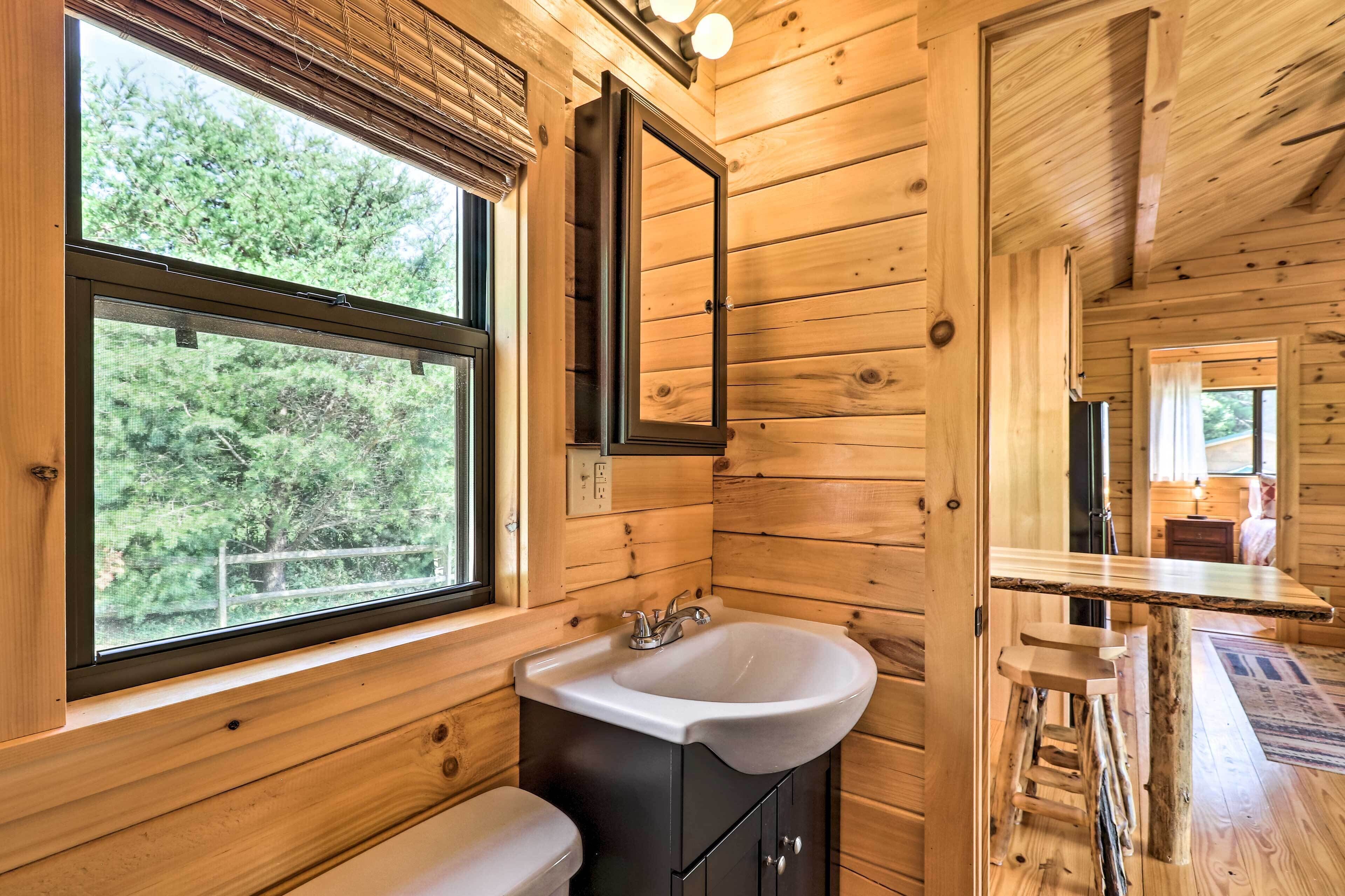 A wooden cabin bathroom with a large window, a sink, and a mirror.