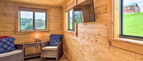 A wooden cabin interior with a sofa, a small table, and a chair. There are two windows providing views of the outdoors.