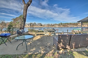 Um pátio externo com mesa e cadeiras, churrasqueira e vista para um lago com edifícios ao fundo.