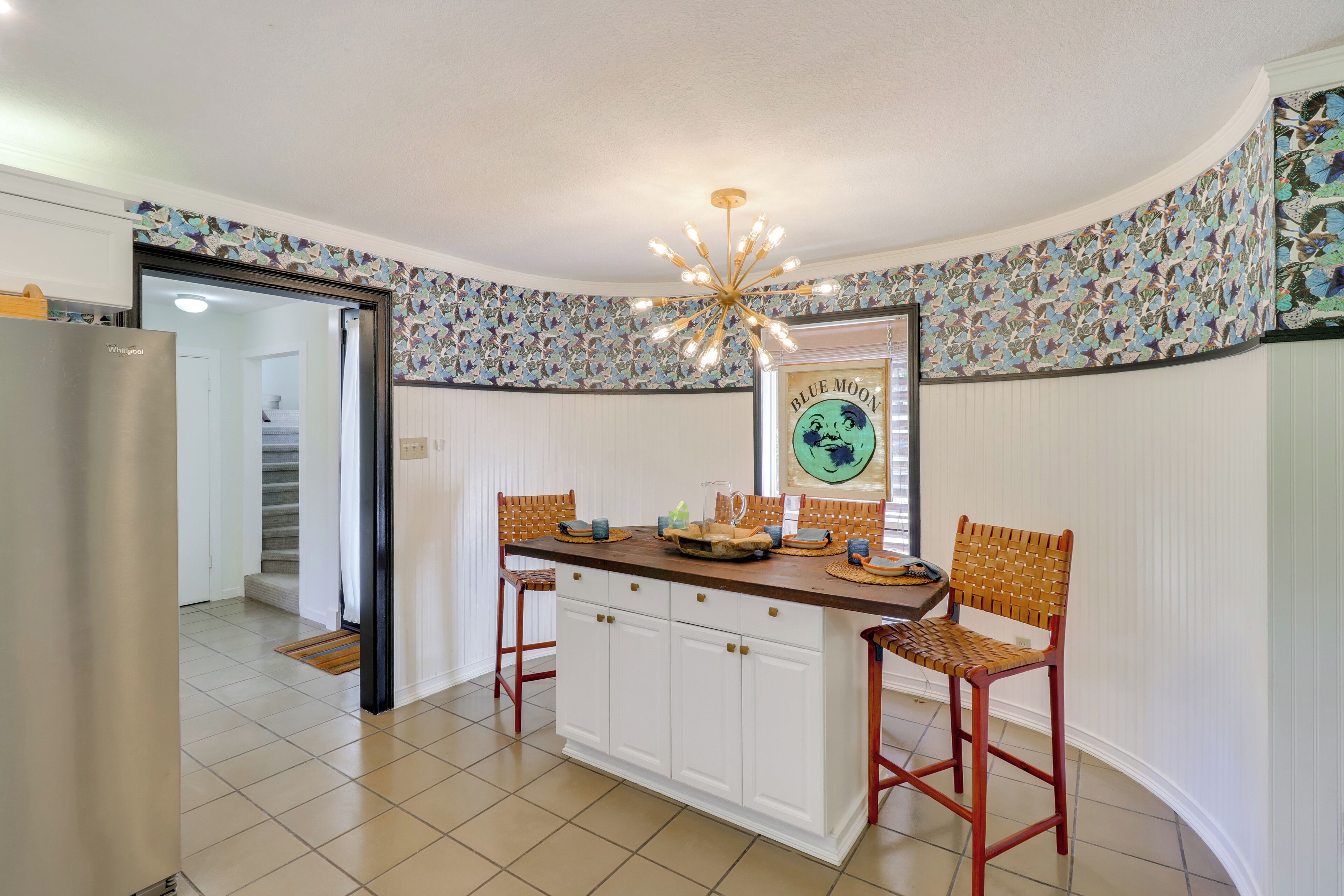 A kitchen with a central island, two wooden chairs, a refrigerator, and a decorative ceiling light.