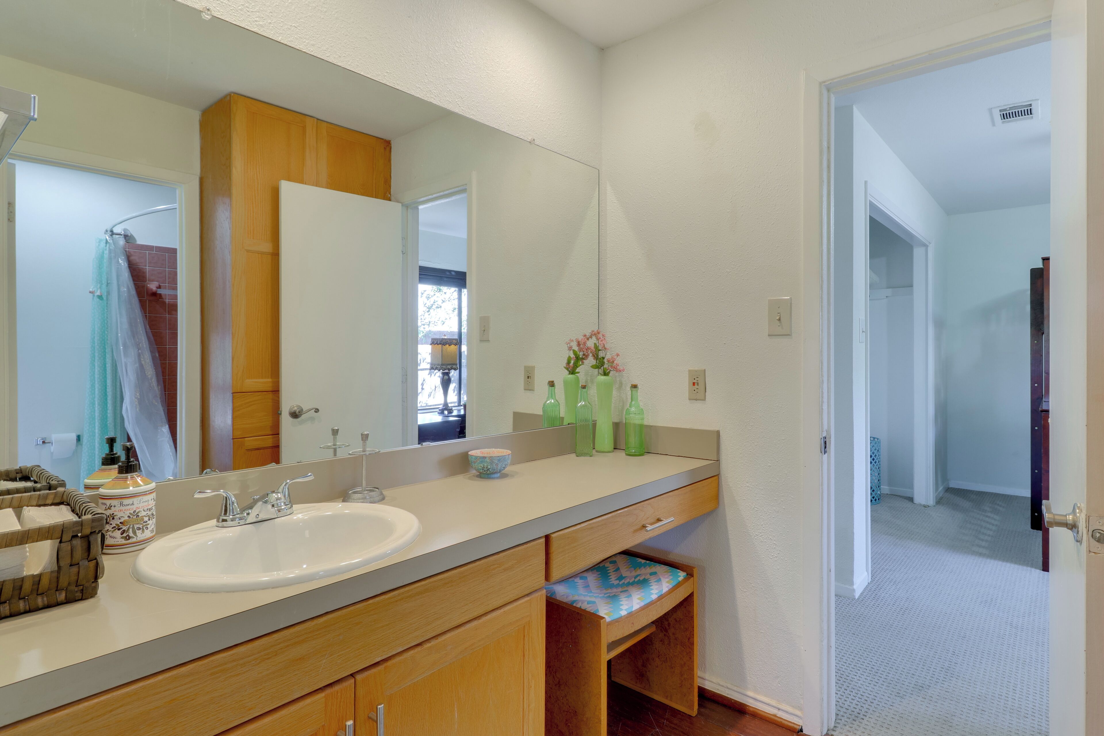 A bathroom with a large mirror, wooden cabinets, a sink, and a shower area.