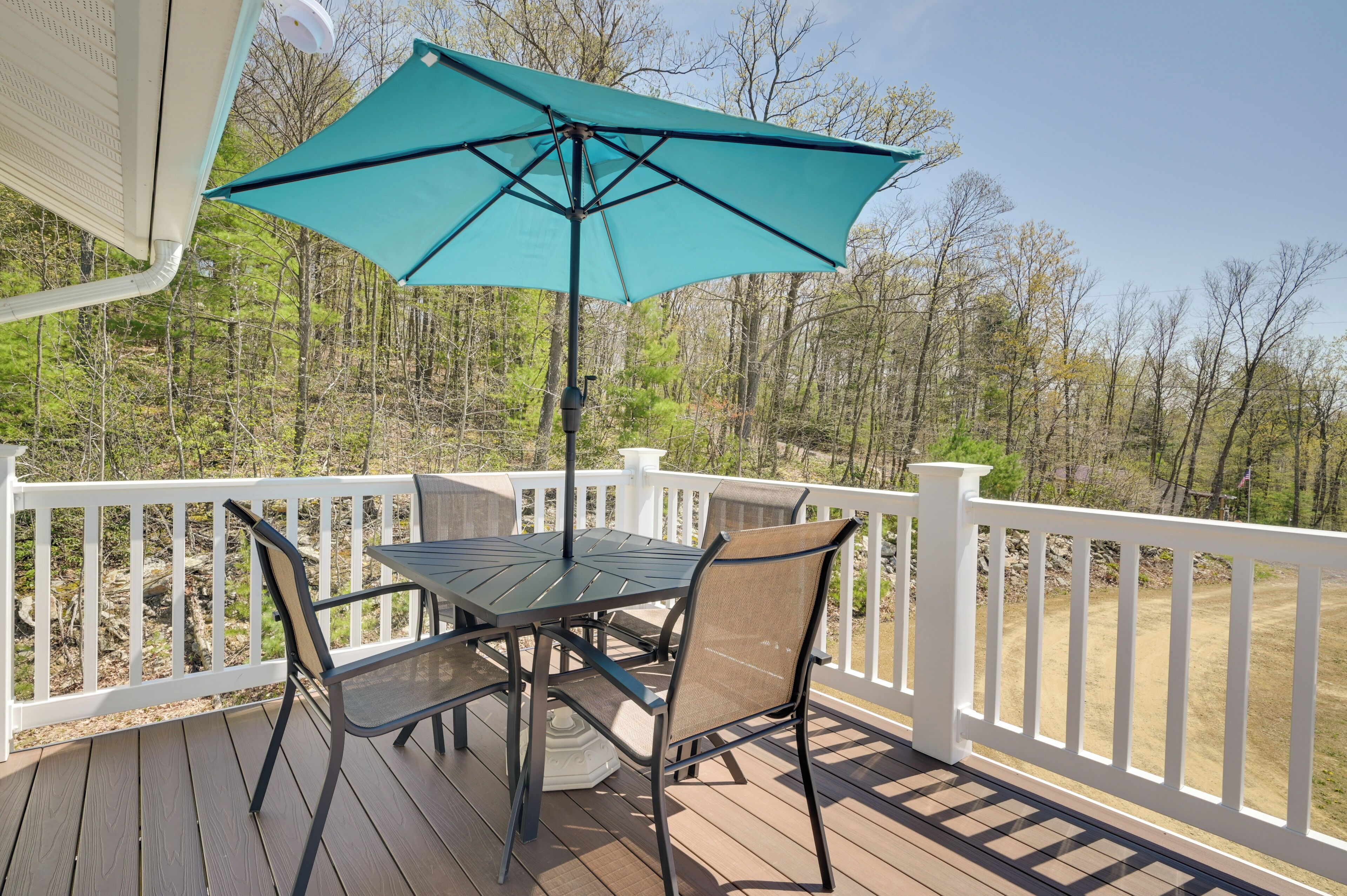 A deck with a table and chairs, a turquoise umbrella, and a white railing.