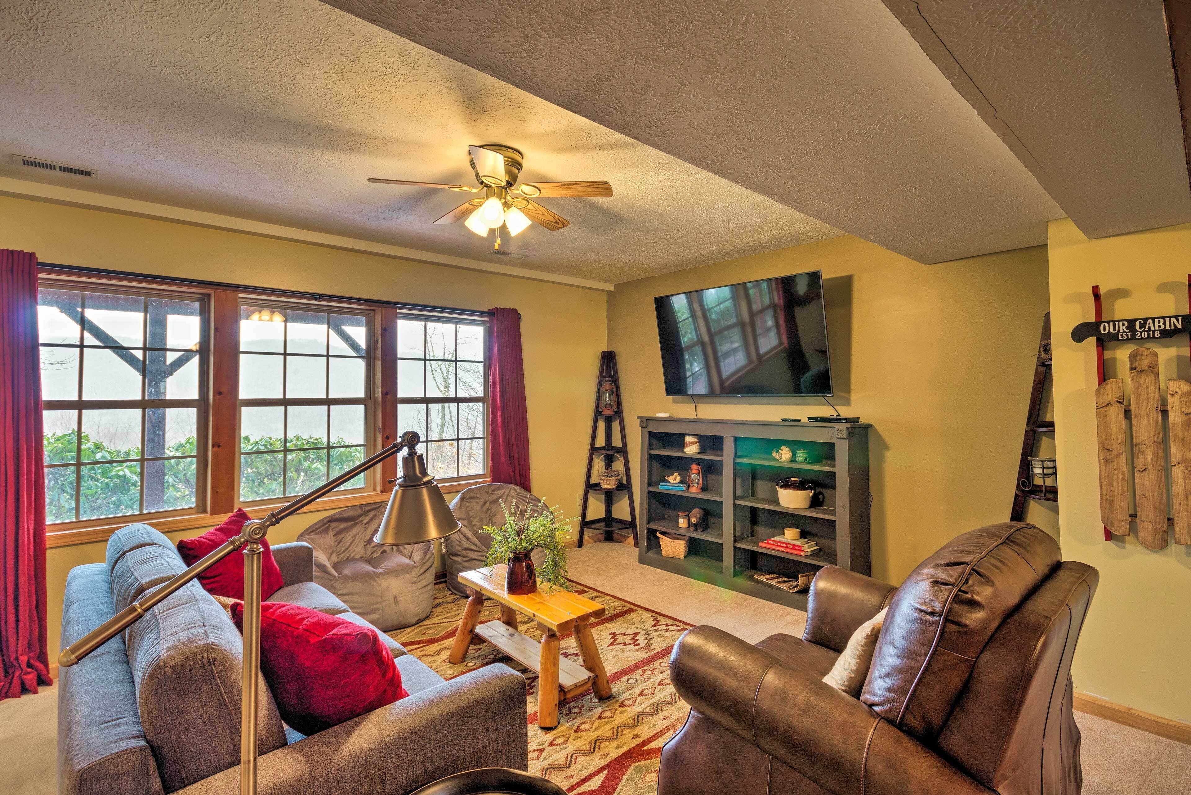 A cozy living room with a ceiling fan, a television, a bookshelf, and a fireplace.