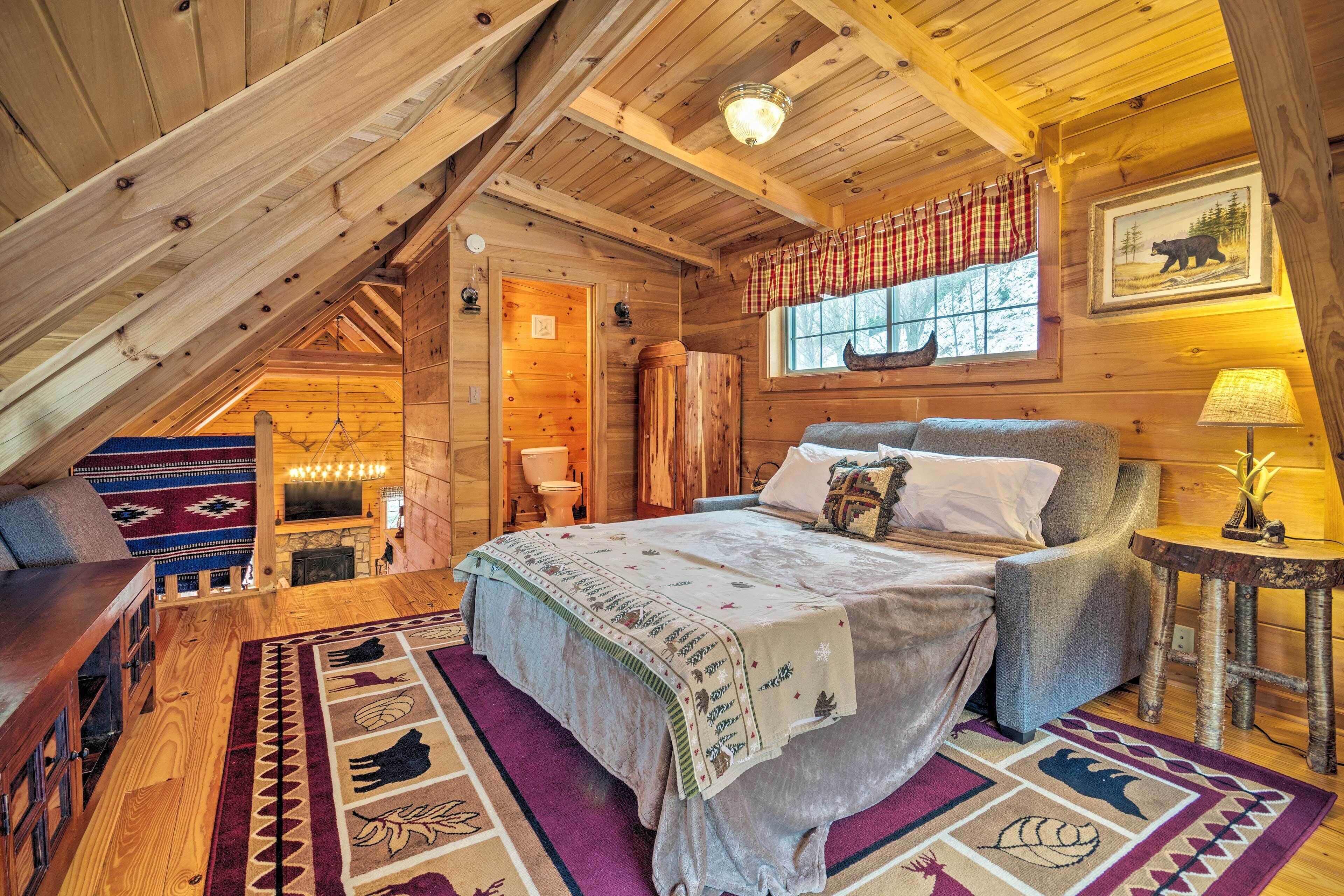 A cozy log cabin bedroom with a bed, a chair, a small table, and a window with a bear painting.