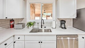 A modern kitchen with white cabinets, a stainless steel sink, a toaster, a coffee maker, and a dishwasher. - On-site Boat Launch: Gun Barrel City Lake House (Mabank)