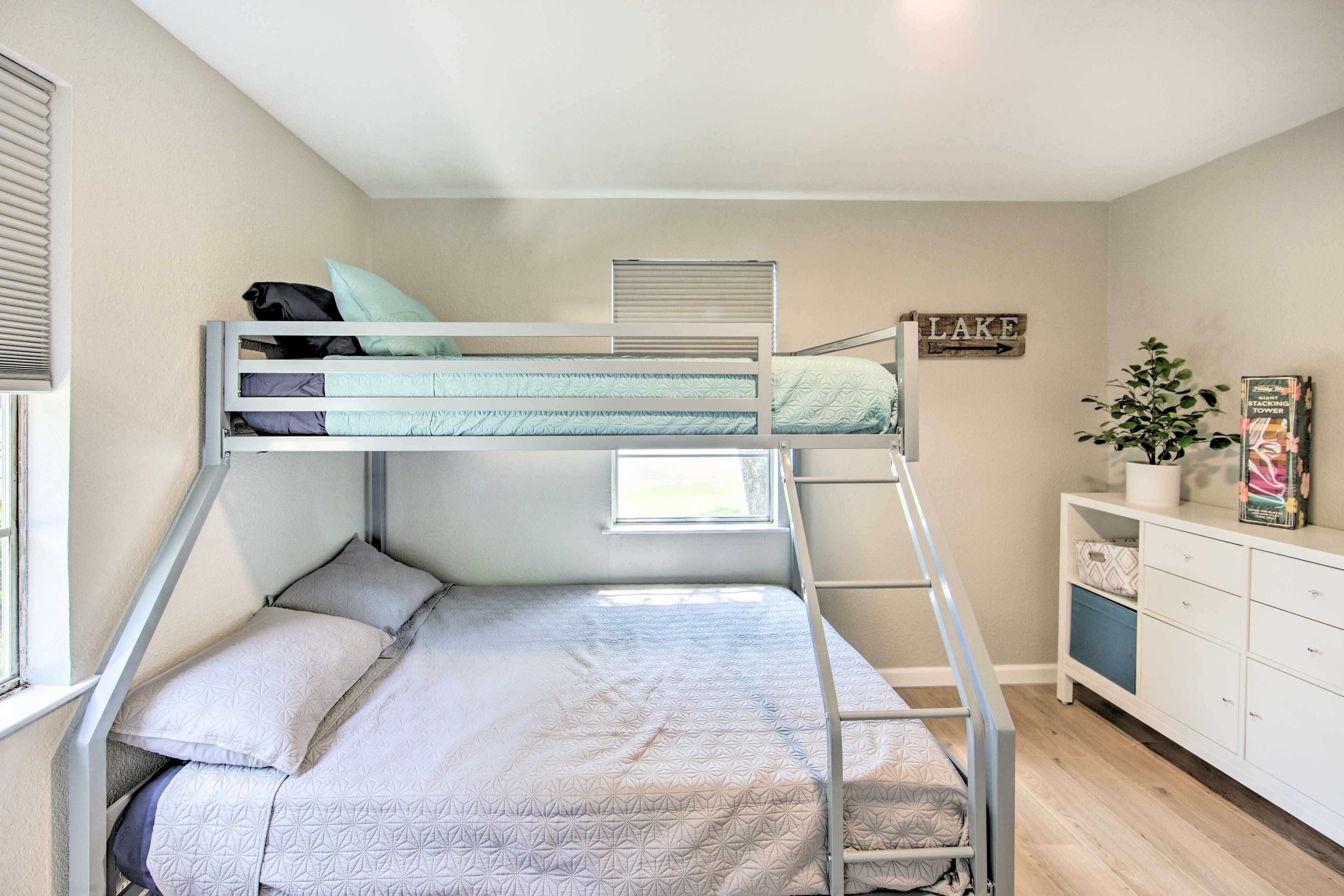 A bunk bed room with a window, a sign that says "LAKE", and a white dresser with drawers.