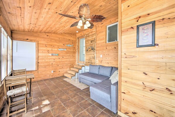A wooden cabin interior with a sofa, a chair, a ceiling fan, and a staircase.