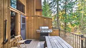 A wooden deck with a grill and a folding chair, surrounded by trees. - Whitefish Escape w/ Deck: 3 Mi to Ski Resort! (Whitefish)