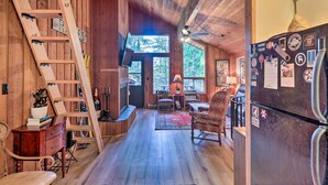 A rustic cabin interior with wooden walls, a wooden ladder, a fireplace, a dining area, and a refrigerator with magnets. - Whitefish Escape w/ Deck: 3 Mi to Ski Resort! (Whitefish)
