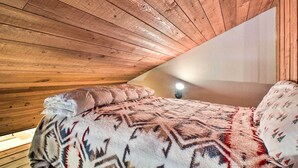 A cozy attic bedroom with wooden slats on the ceiling, a bed with patterned bedding, and a wall-mounted light. - Whitefish Escape w/ Deck: 3 Mi to Ski Resort! (Whitefish)
