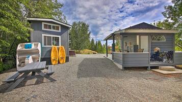 A small cabin with a covered porch, a picnic table, and kayaks stored outside.