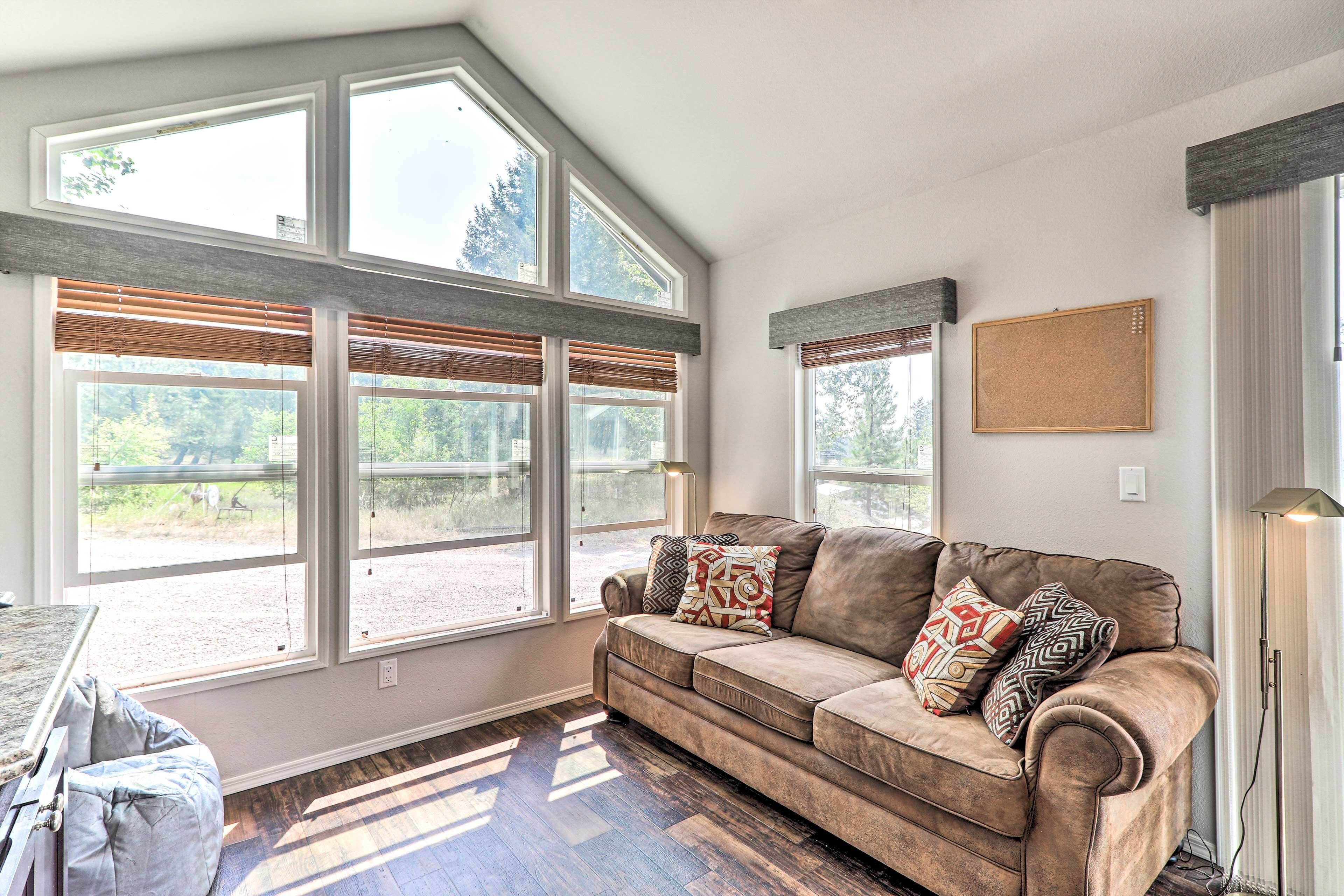 A cozy living room with a large window, a brown sofa, and a floor lamp.