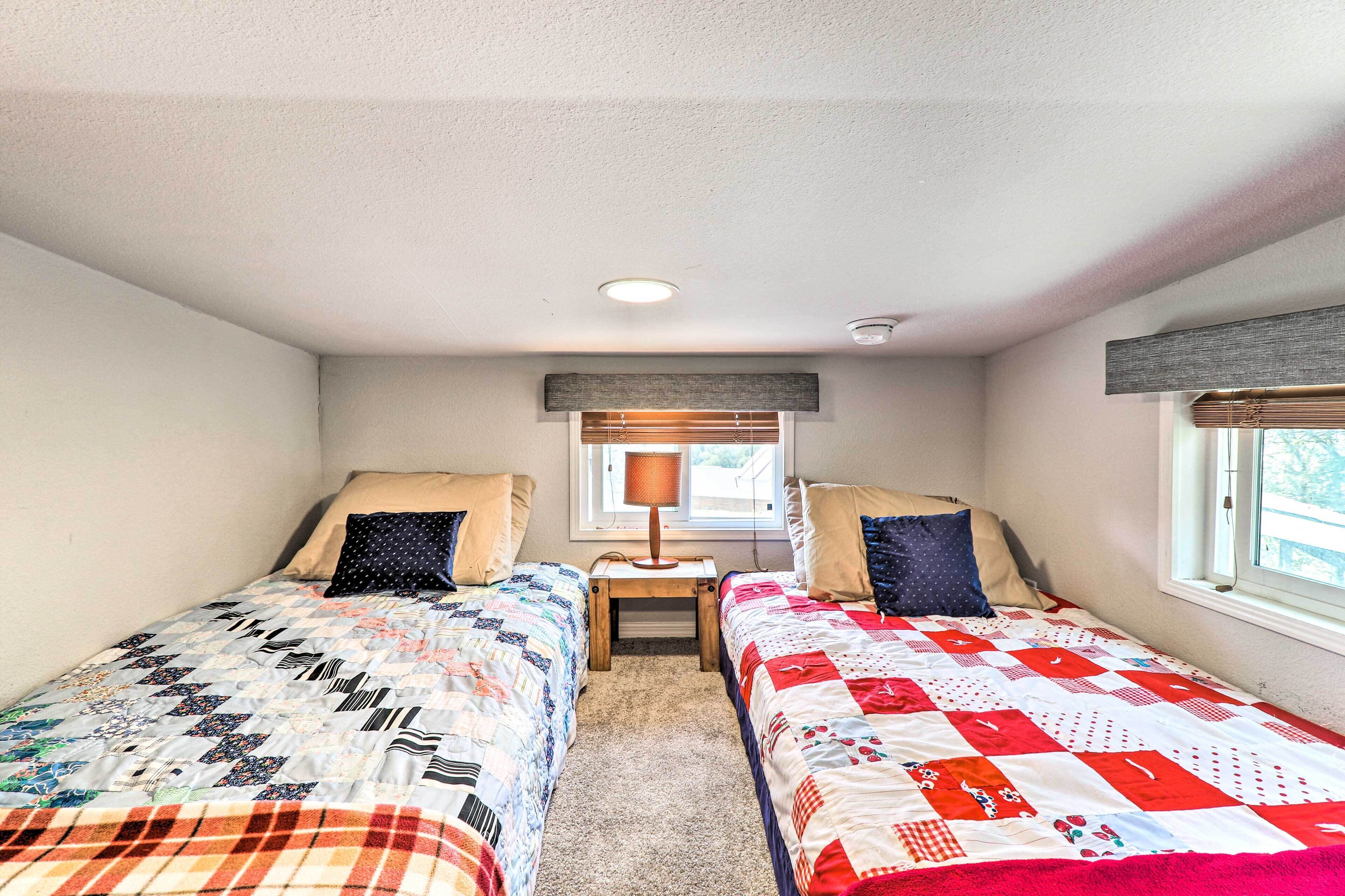 A bedroom with two single beds, a nightstand with a lamp, a window with blinds, and a ceiling light.
