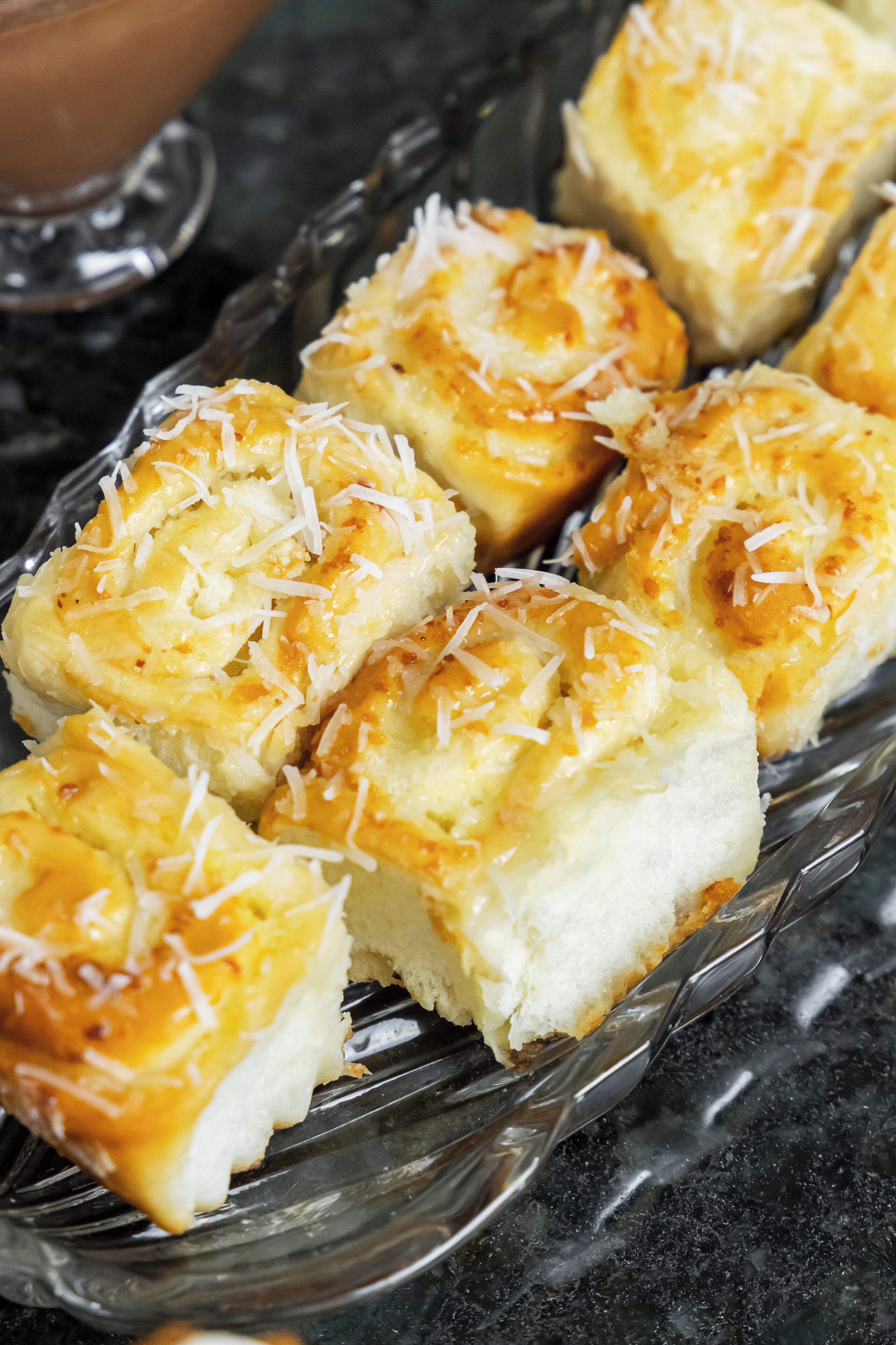 A glass dish with several pieces of bread topped with cheese and shredded coconut.